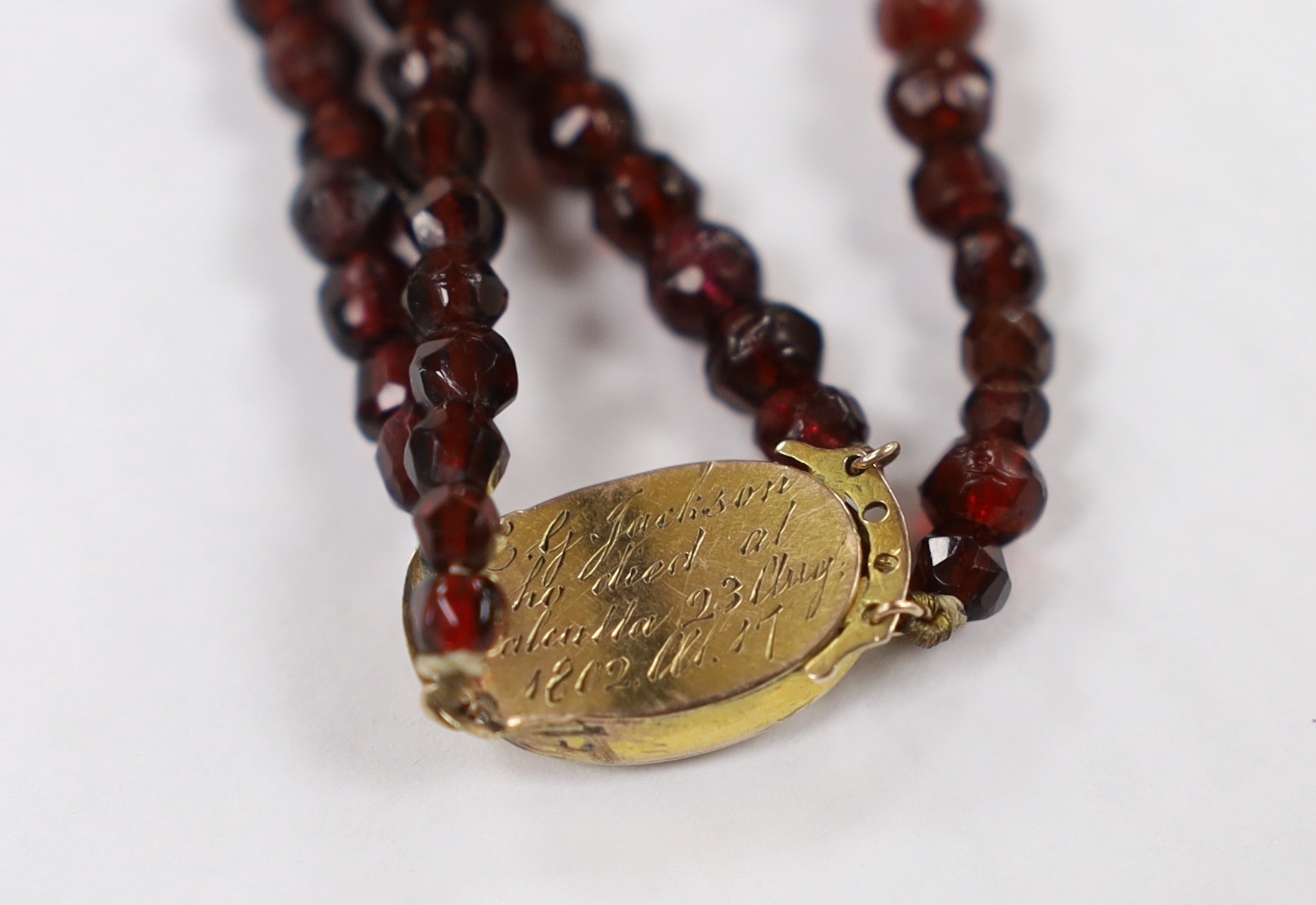 A George III twin strand facetted red paste? necklace, with yellow metal and plaited hair clasp, engraved,' E.G. Jackson who died at Calcutta, 23rg Aug. 1802 at 17', 40cm and a pair of 18k yellow metal and cabochon star